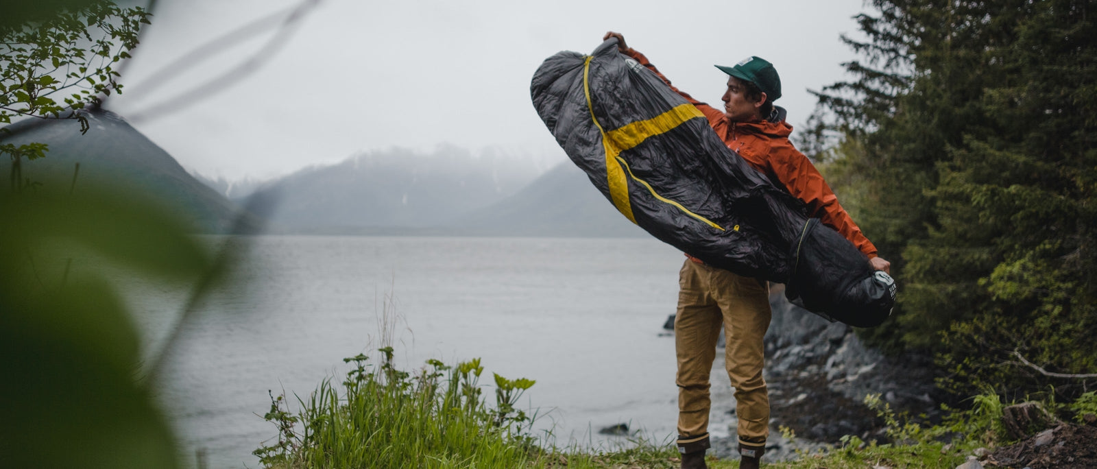 Backpacker pulls Sierra Designs Nitro sleeping bag from its stuff-sack as he sets up a lakeside camp