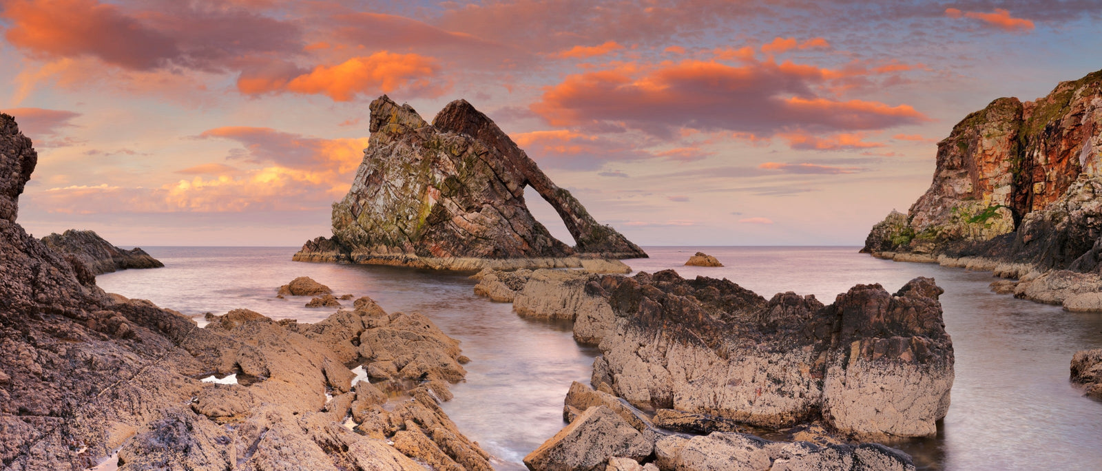 Bow Fiddle Rock, a natural rock arch on the Moray coast, Scotland, at sunset.