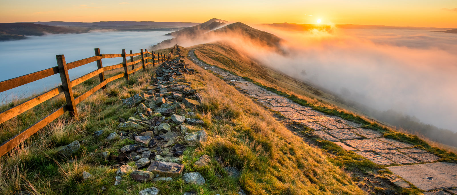 Thick cloud inversion with morning sun casting golden light on the landscape at Mam Tor in the Peak District.