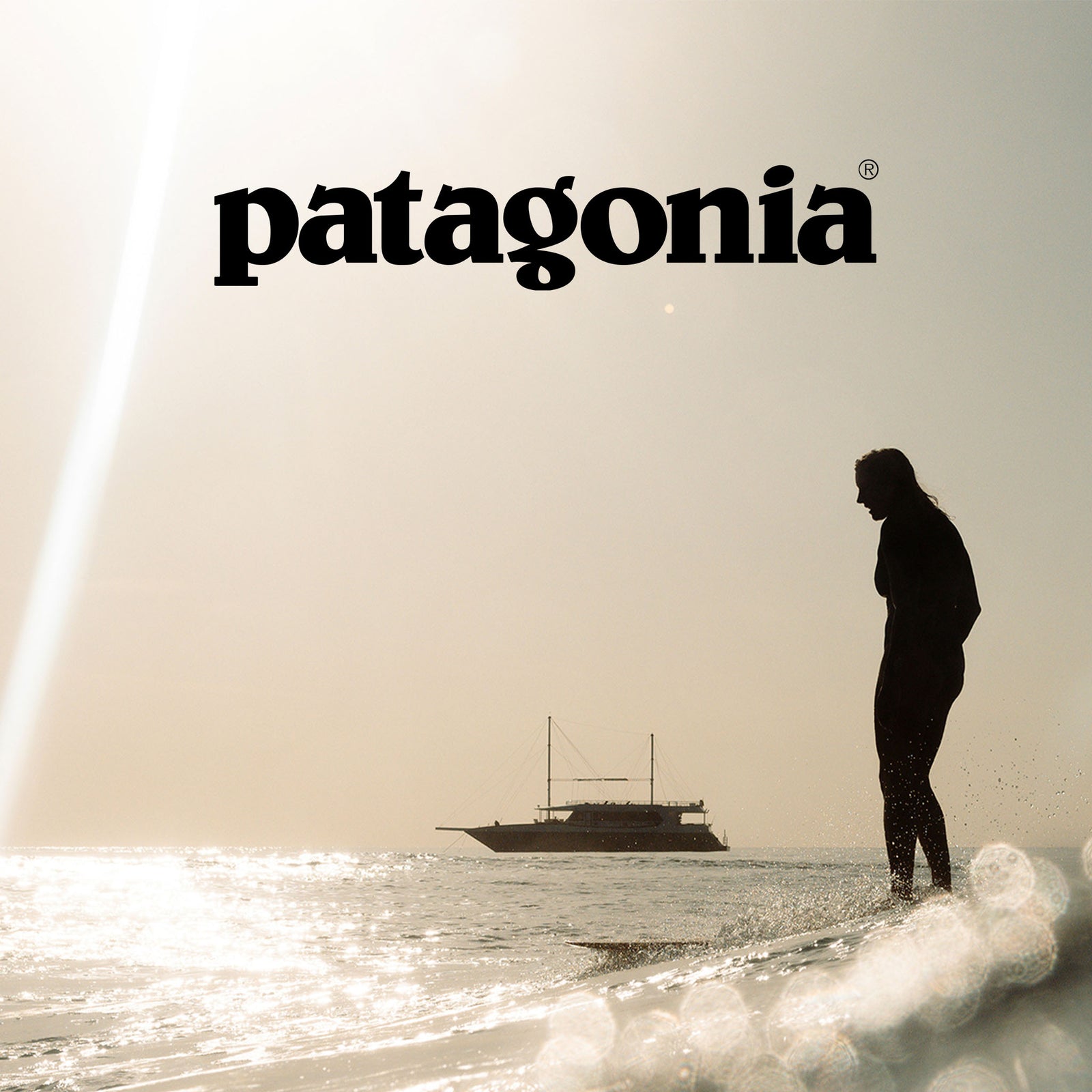 Patagonia logo above a silhouetted woman wading in the sea with a sailing boat beyond.
