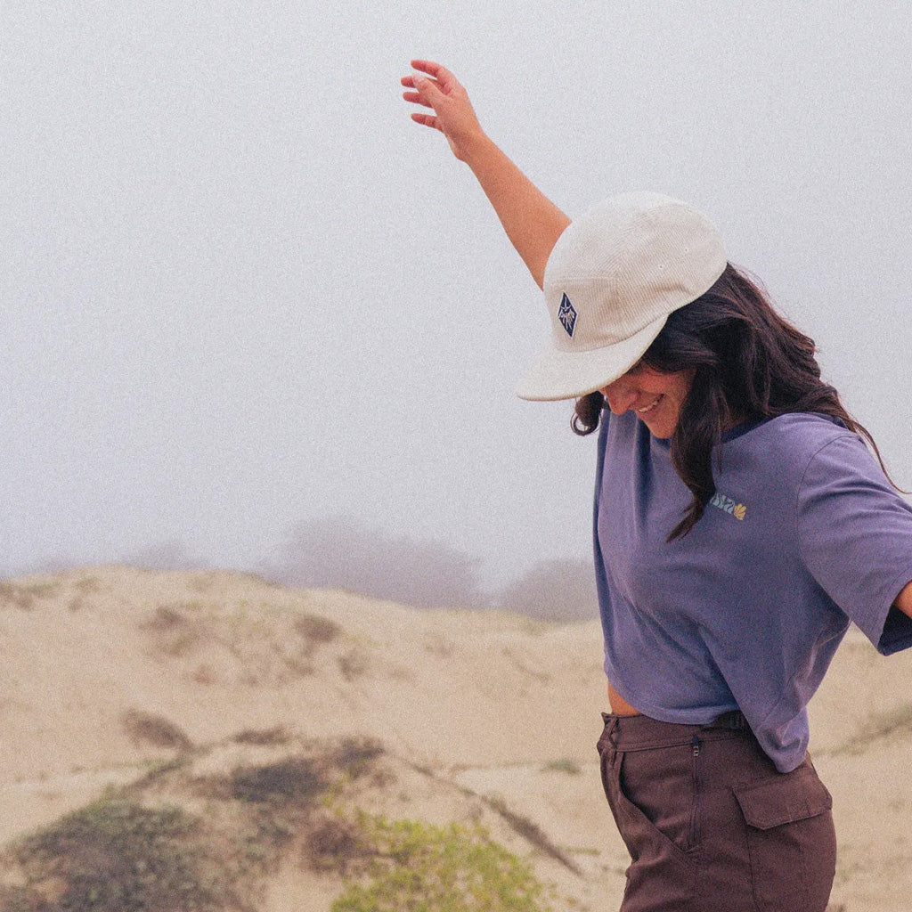 A person wearing a white sun hat and purple fleece jacket on a misty moorland landscape.