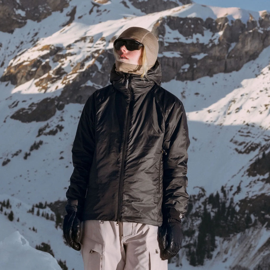 Woman in black Houdini jacket and white snow trousers on snowy mountain slope.