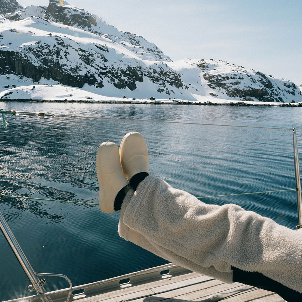Person wearing white Fubuki boots relaxing on a boat deck overlooking snow-capped mountains and arctic waters.
